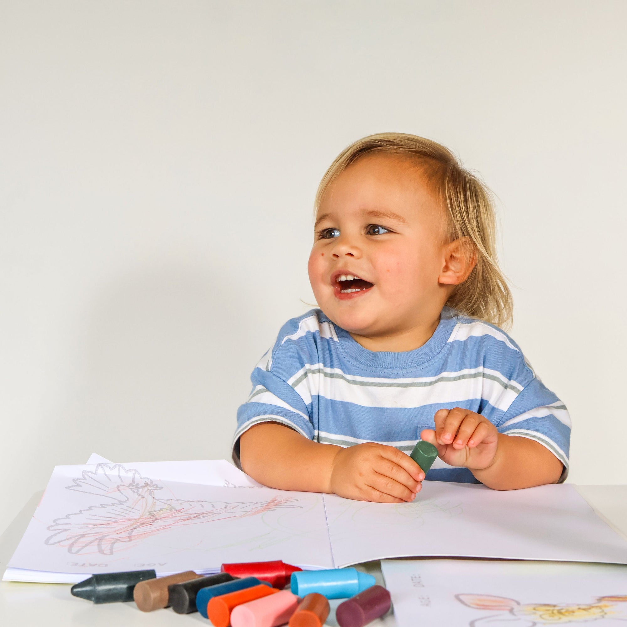 Child sitting at a table with drawing materials, smiling.